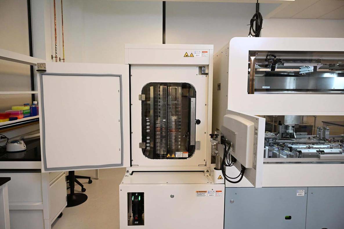 Interior of the NPi-11 automated cell culture machine with the integrated incubator door open, revealing stacked cell culture plates on shelves alongside the enclosed robotic workspace.