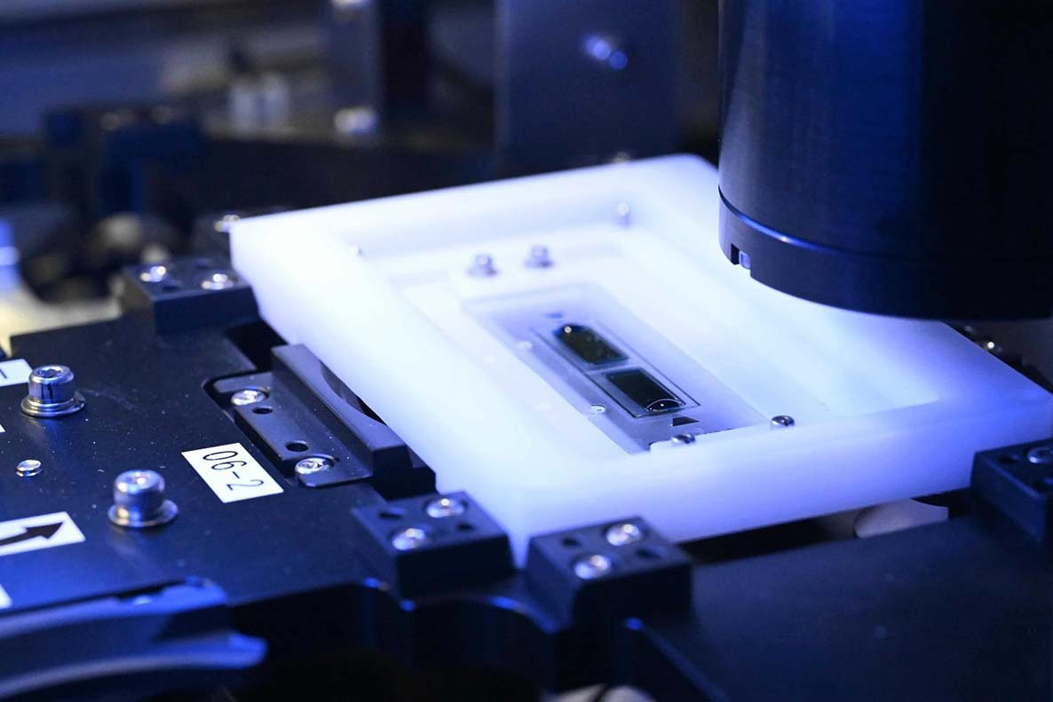 Close-up of the NPi-11 automated cell culture equipment's integrated imaging station with a cell culture vessel on a backlit stage and microscope objective positioned for analysis.