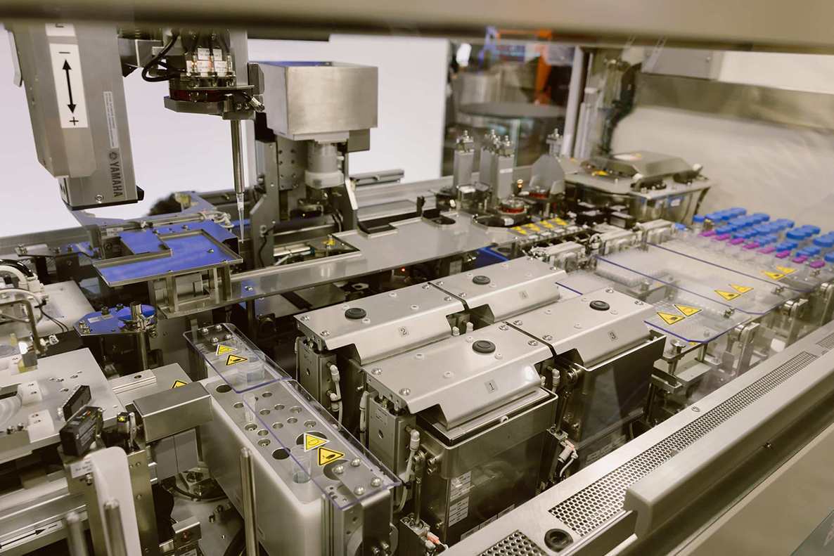 Interior workspace of the NPi-11 automated cell culture system showing the robotic pipetting arm, cell culture dishes on plate holders, centrifuge tubes with blue and pink caps, and pipette tip racks.